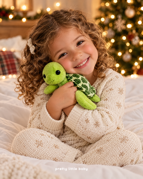Girl hugging Turtle Buddy plush by the Christmas tree